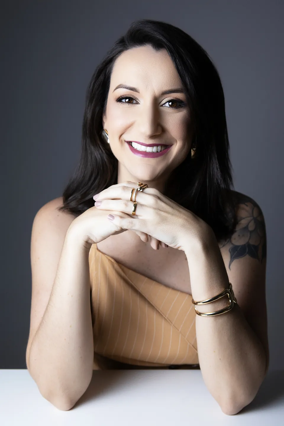 Julia Poltronieri sorrindo, com as mãos entrelaçadas sobre a mesa